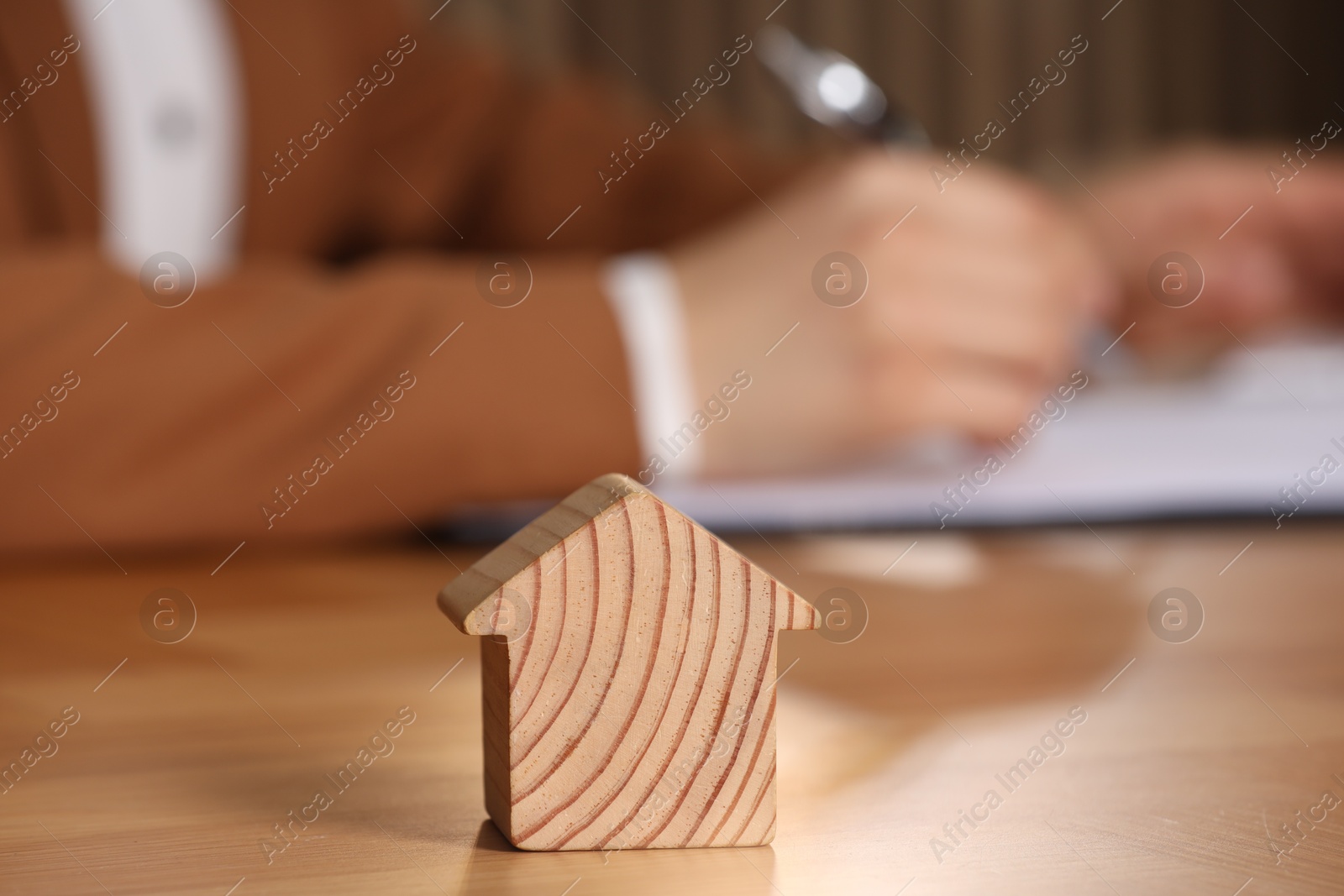 Photo of Property insurance. Real estate agent working at table indoors, focus on wooden house figure