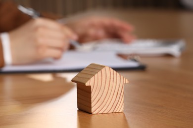 Photo of Property insurance. Real estate agent working at table indoors, focus on wooden house figure