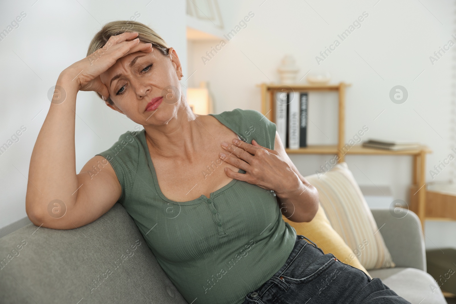 Photo of Menopause. Woman suffering from hot flash on sofa indoors