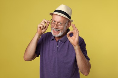 Portrait of handsome senior man showing ok gesture on yellow background