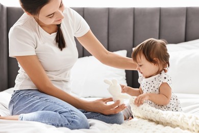 Photo of Beautiful young mother and her cute little baby with rabbit toy on bed at home