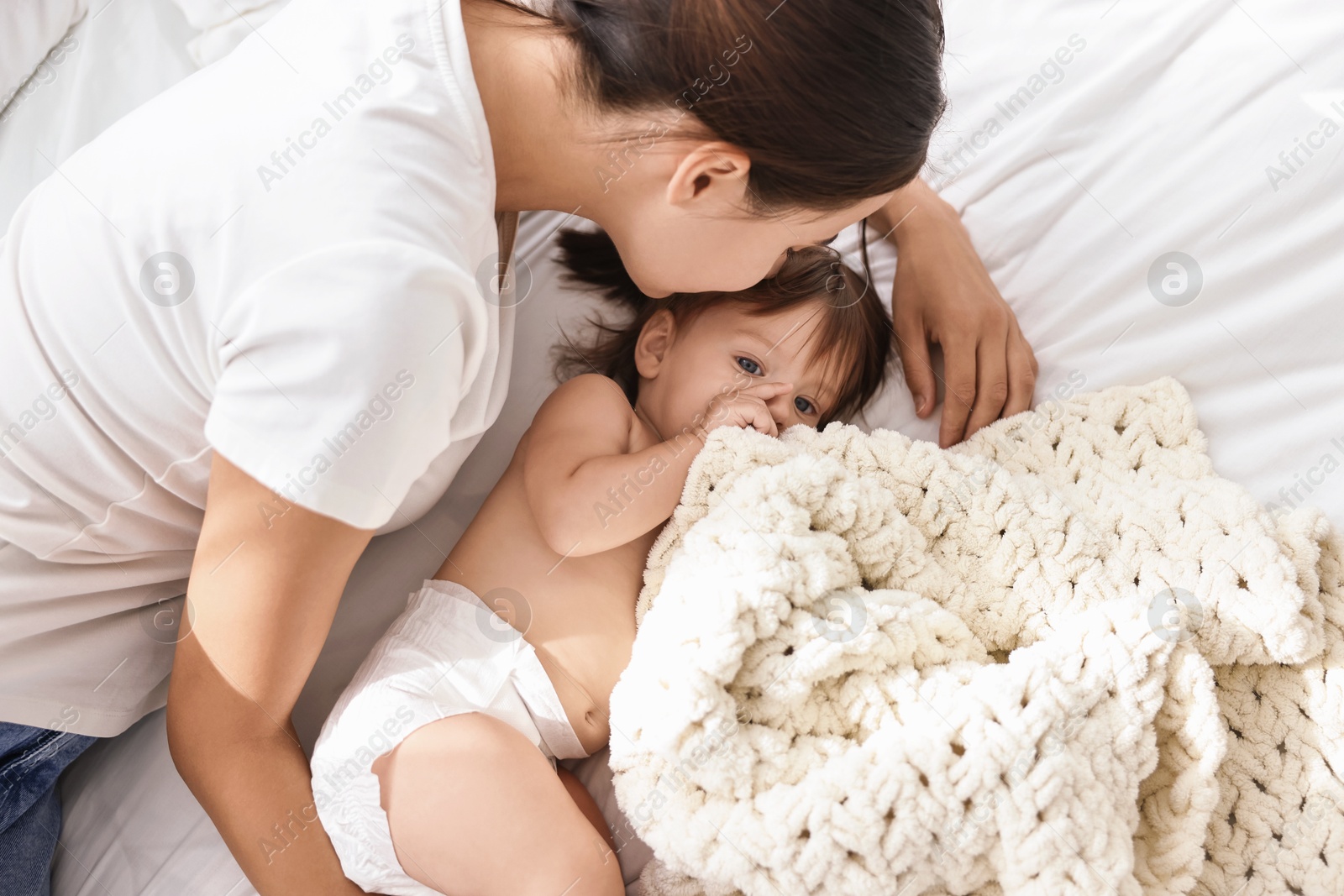 Photo of Beautiful young mother with her cute little baby on soft bed, top view