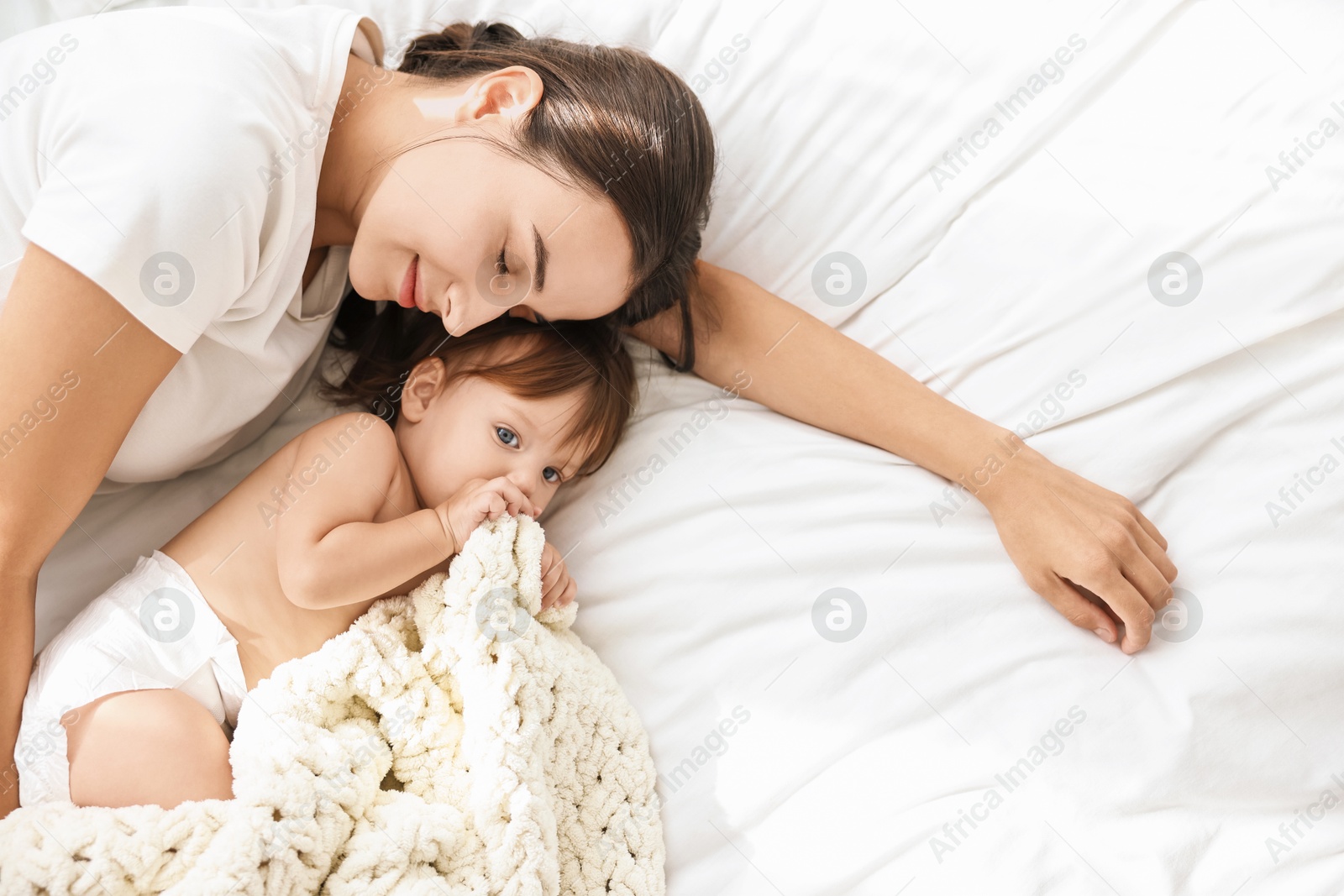 Photo of Beautiful young mother with her cute little baby on soft bed, top view