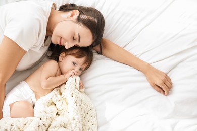 Beautiful young mother with her cute little baby on soft bed, top view