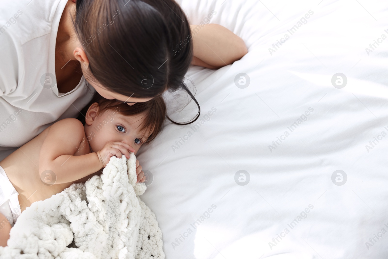 Photo of Young mother with her cute little baby on bed, above view