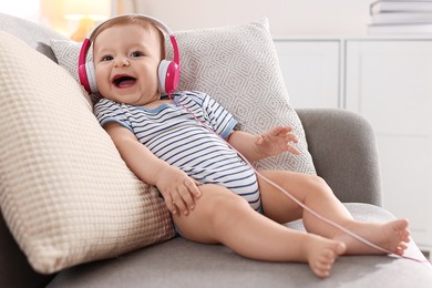 Photo of Cute little baby with headphones on sofa at home