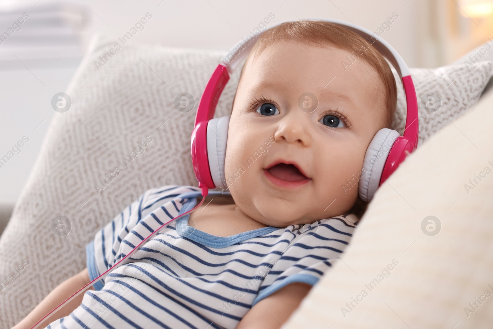 Photo of Cute little baby with headphones on sofa at home