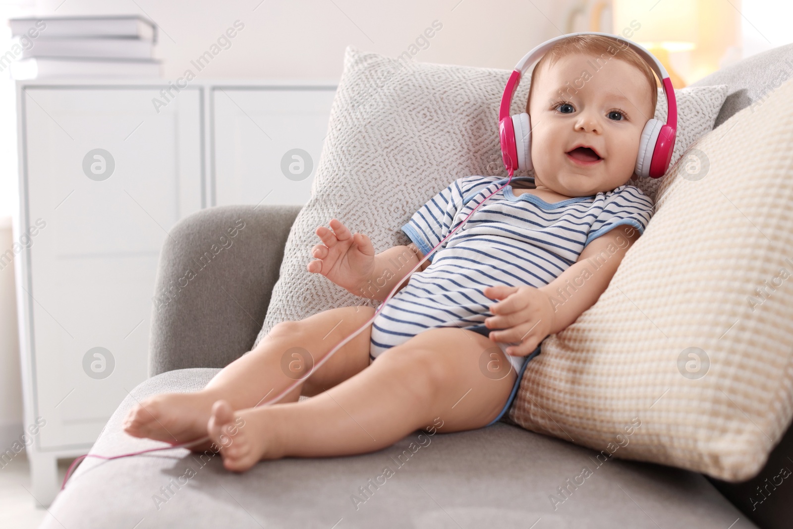 Photo of Cute little baby with headphones on sofa at home