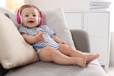 Cute little baby with headphones on sofa at home, space for text