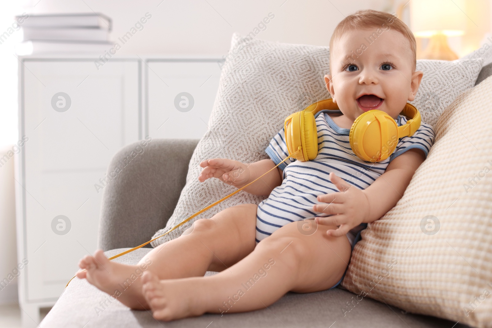 Photo of Cute little baby with headphones on sofa at home, space for text