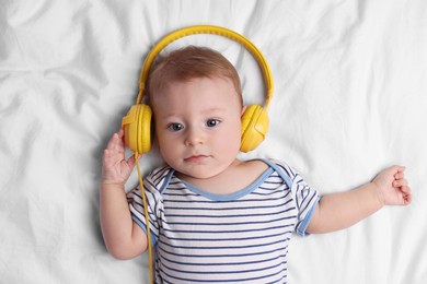 Cute little baby with headphones lying on bed, top view