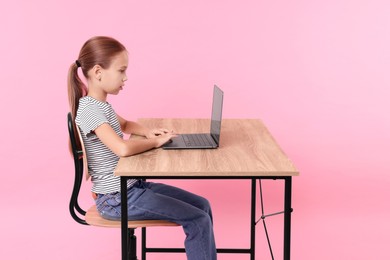 Girl with correct posture using laptop at wooden desk on pink background