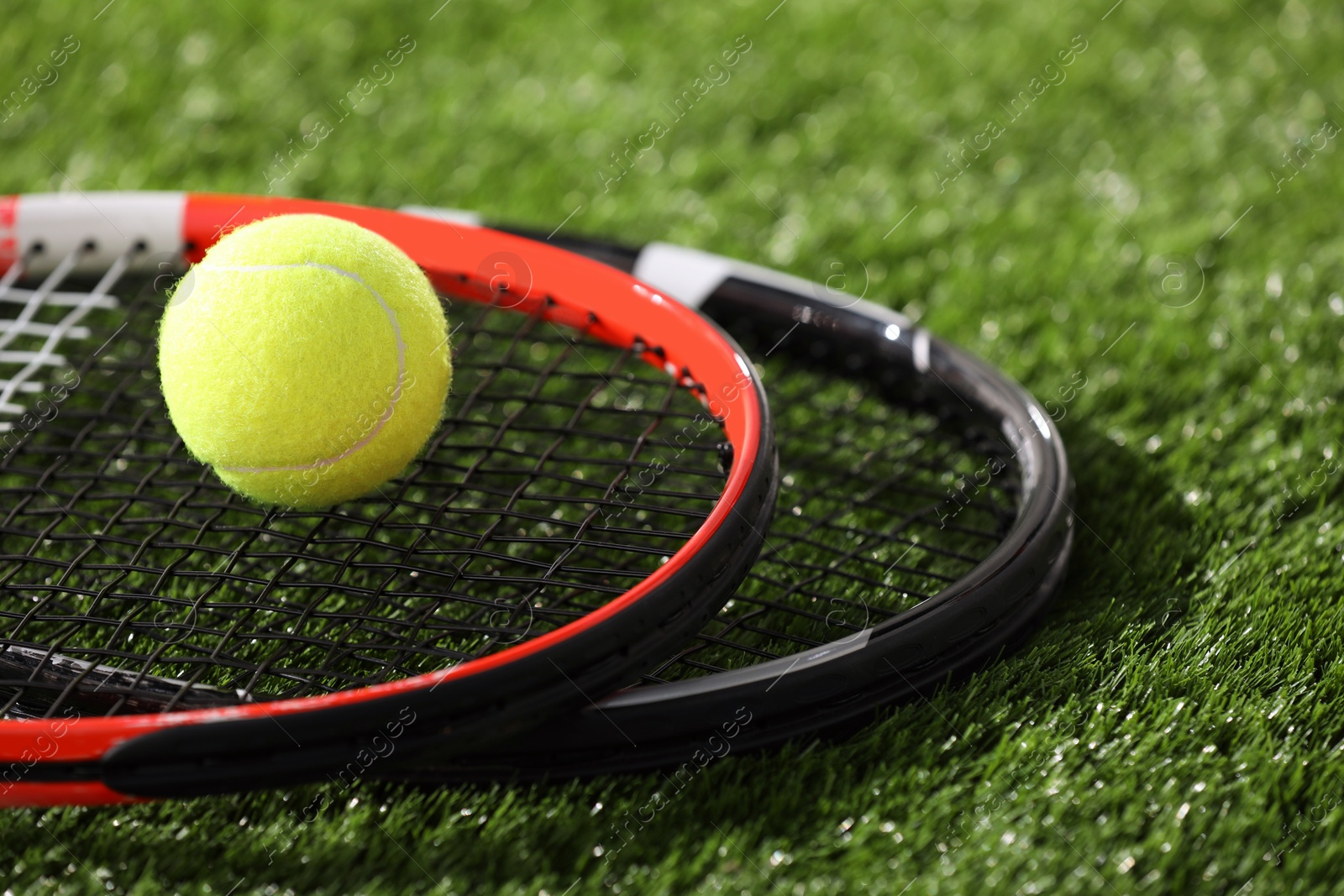 Photo of Tennis rackets and ball on green artificial grass, closeup