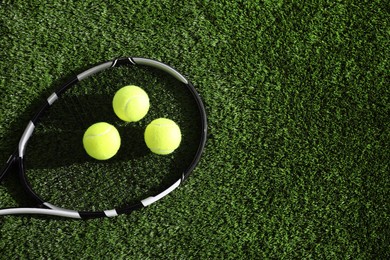 Photo of Tennis racket and balls on green artificial grass, flat lay. Space for text