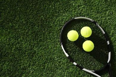 Photo of Tennis racket and balls on green artificial grass, flat lay. Space for text