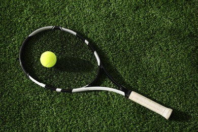 Photo of Tennis racket and balls on green artificial grass, top view