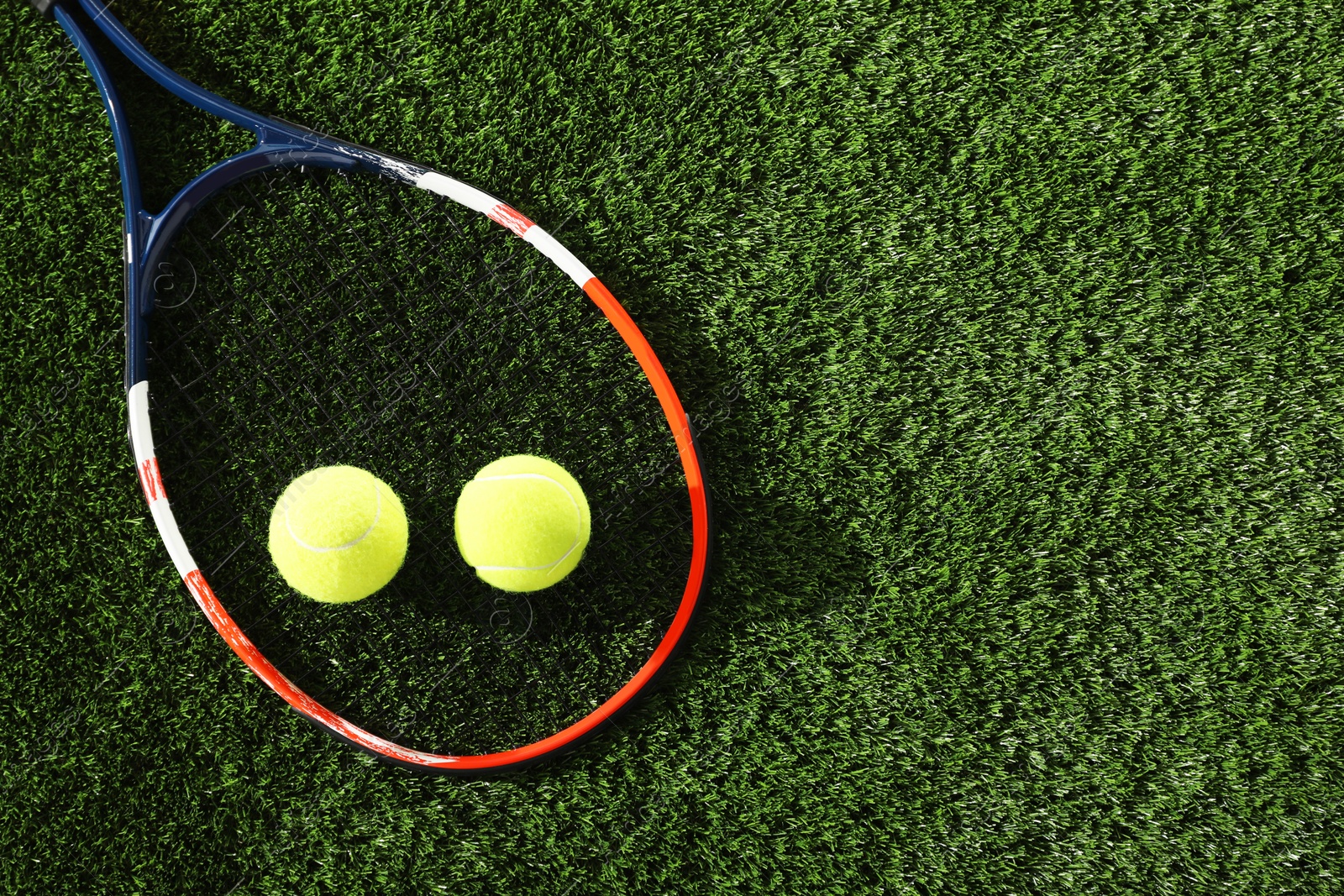 Photo of Tennis racket and balls on green artificial grass, flat lay. Space for text