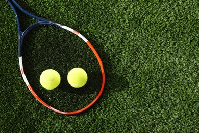 Photo of Tennis racket and balls on green artificial grass, flat lay. Space for text