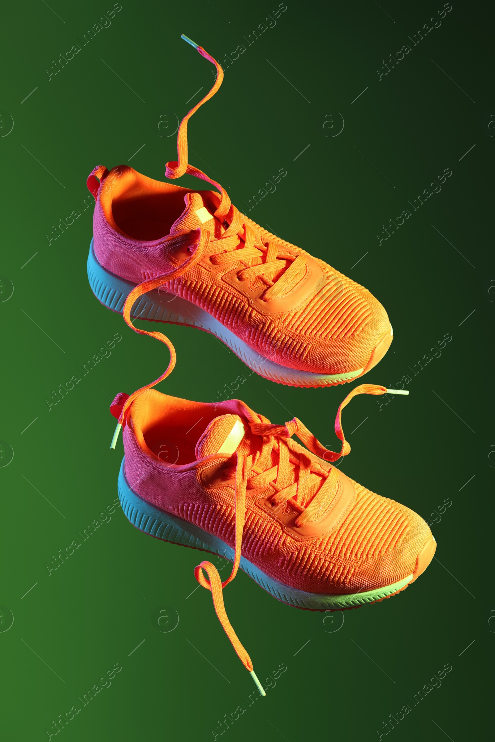 Photo of Pair of stylish sneakers in air against dark green background