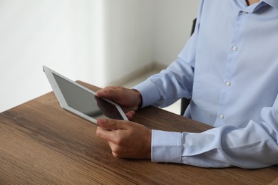 Photo of Businessman using tablet at wooden table, closeup. Modern technology