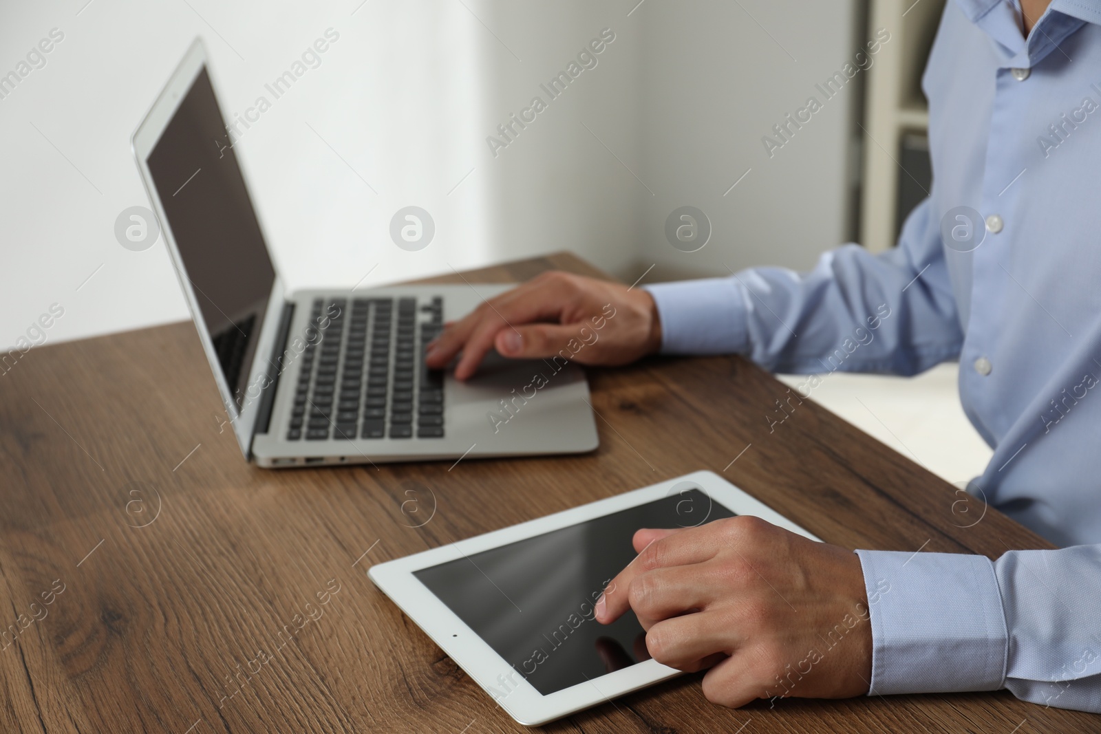 Photo of Businessman using laptop and tablet at wooden table, closeup. Modern technology