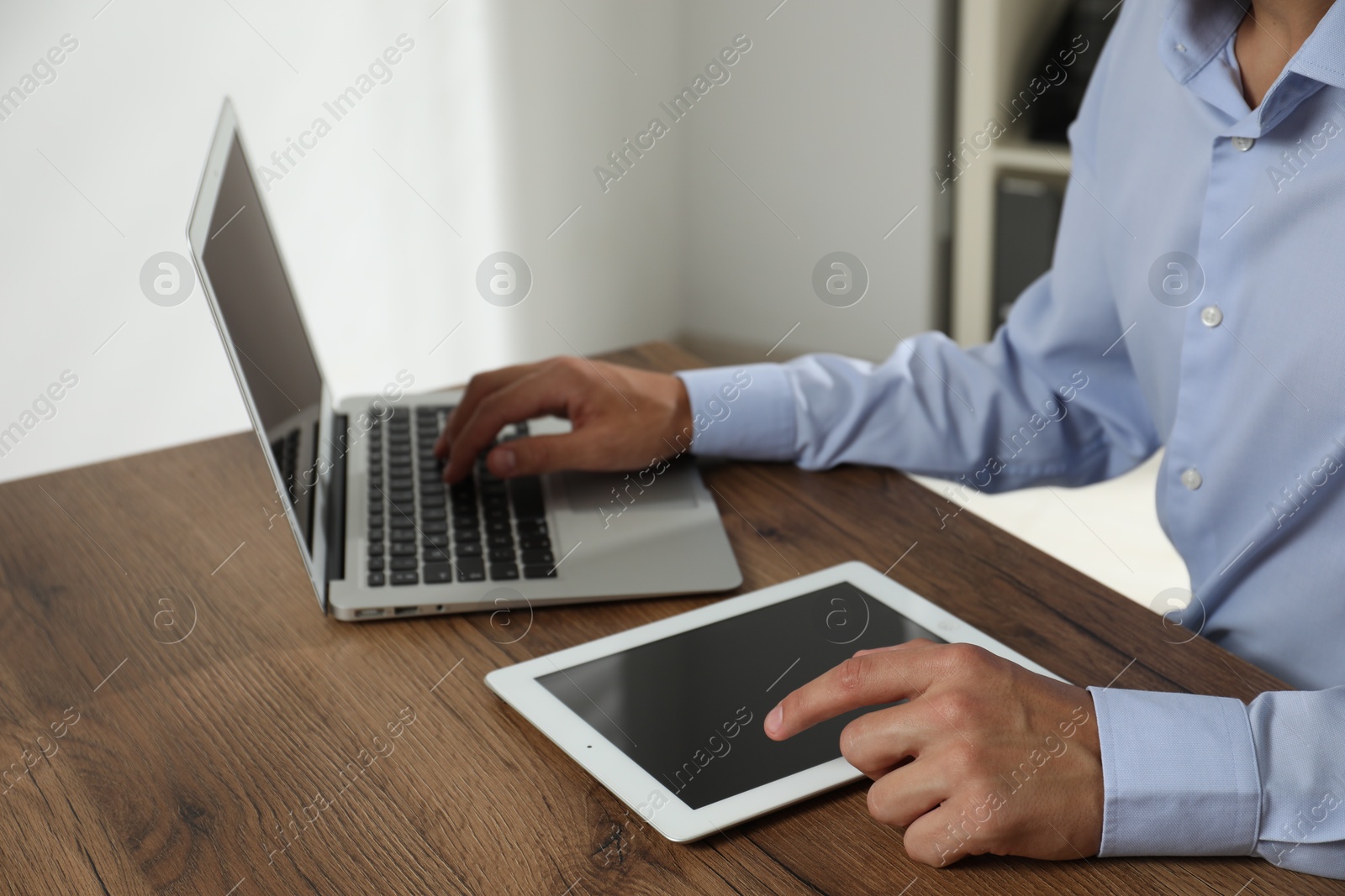 Photo of Businessman using laptop and tablet at wooden table, closeup. Modern technology