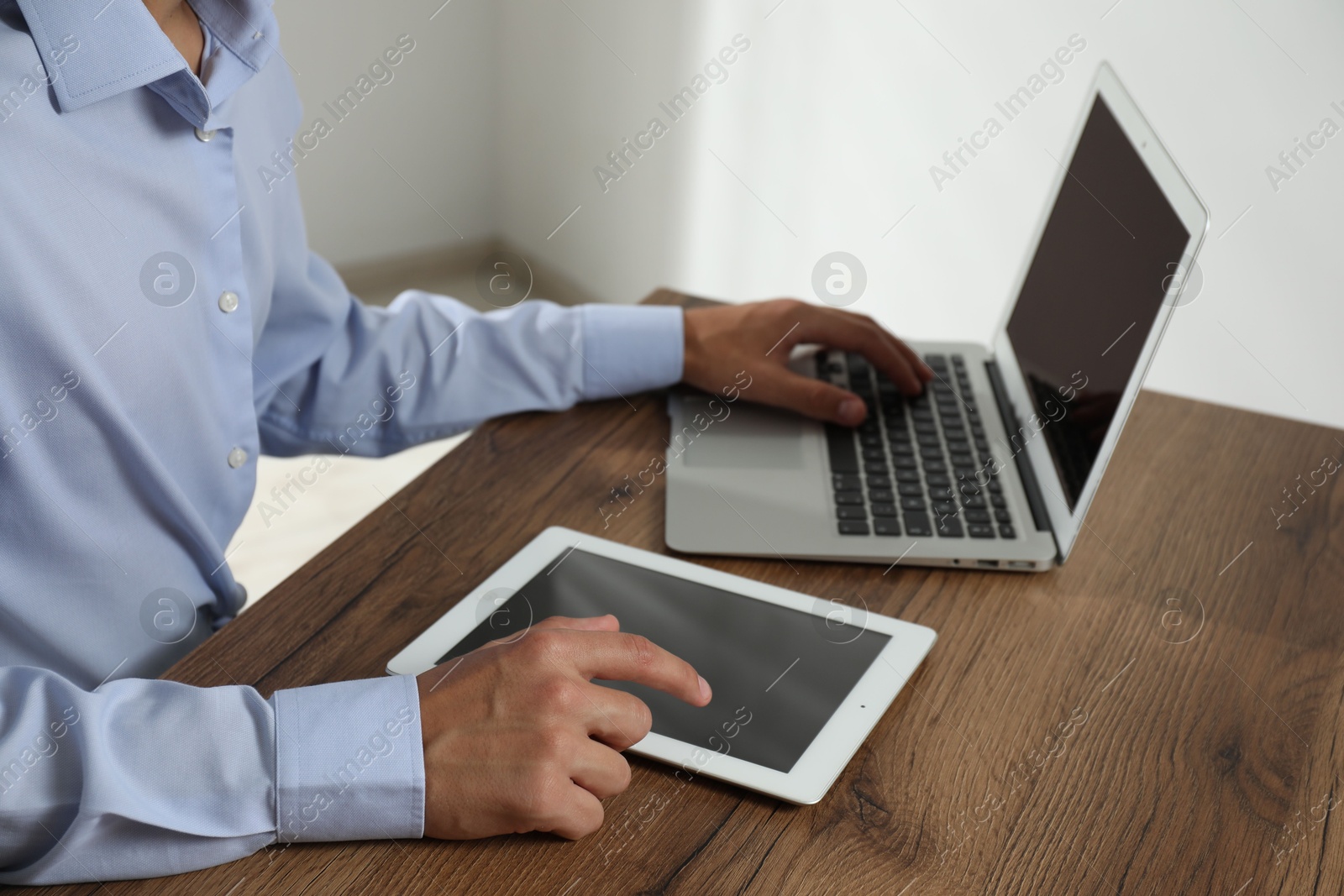 Photo of Businessman using laptop and tablet at wooden table, closeup. Modern technology