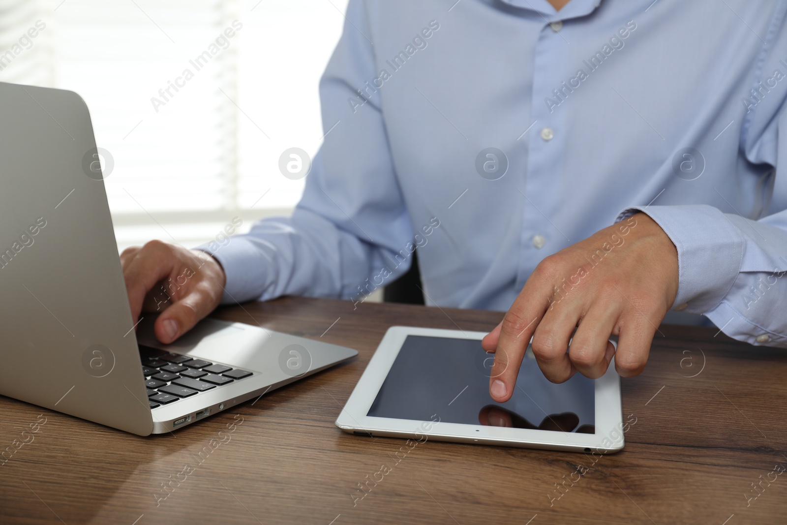 Photo of Businessman using laptop and tablet at wooden table, closeup. Modern technology