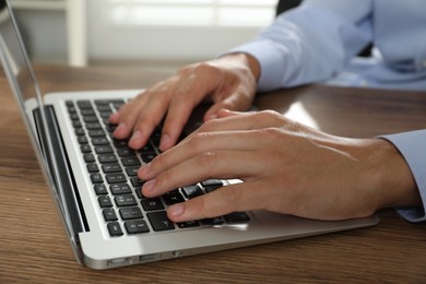 Photo of Businessman using laptop at wooden table, closeup. Modern technology