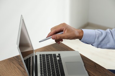 Photo of Businessman with pen near laptop at wooden table, closeup. Modern technology