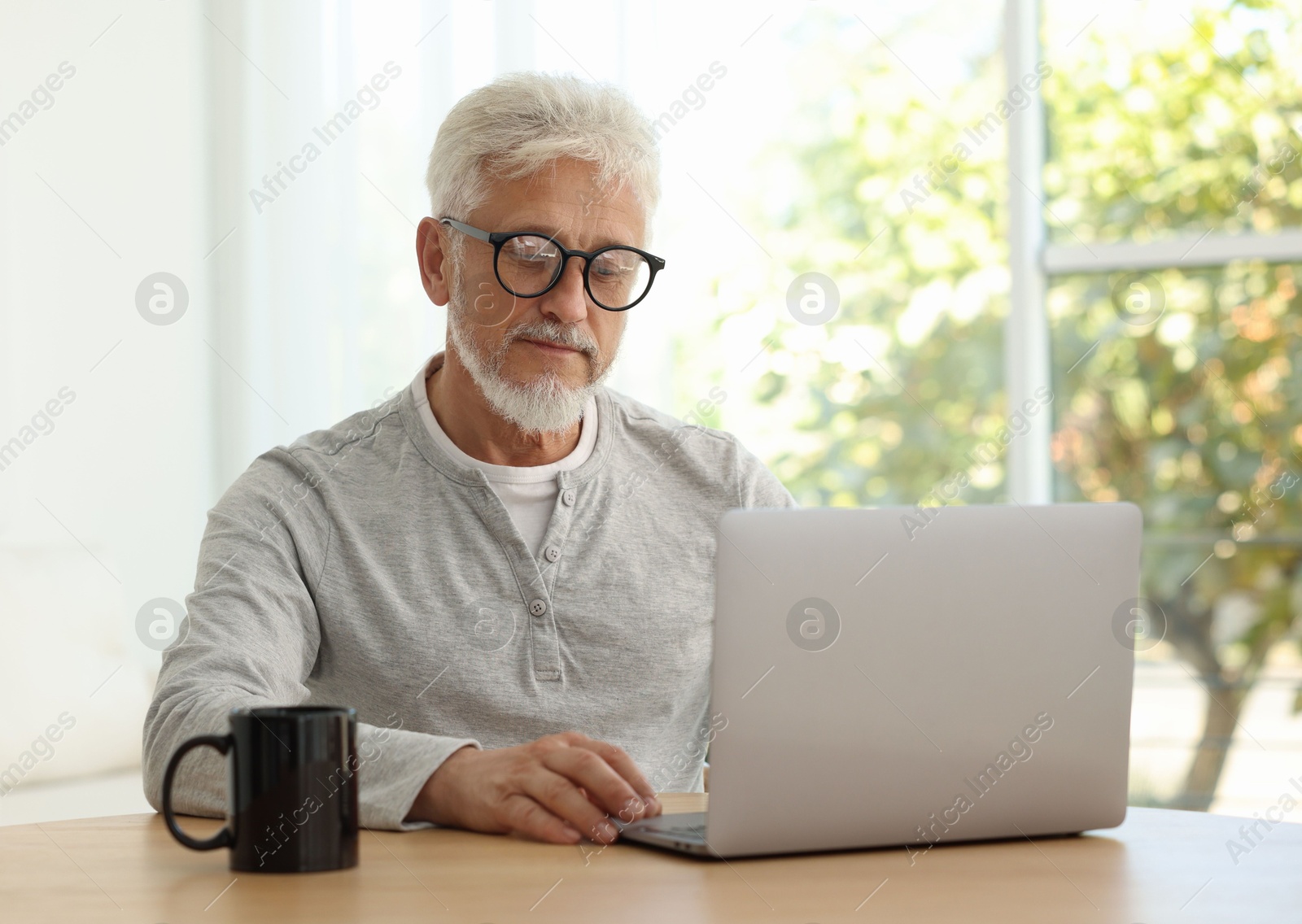 Photo of Senior man using laptop at table indoors