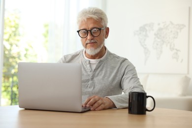 Photo of Senior man using laptop at table indoors