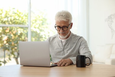 Senior man using laptop at table indoors