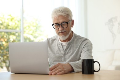 Photo of Senior man using laptop at table indoors