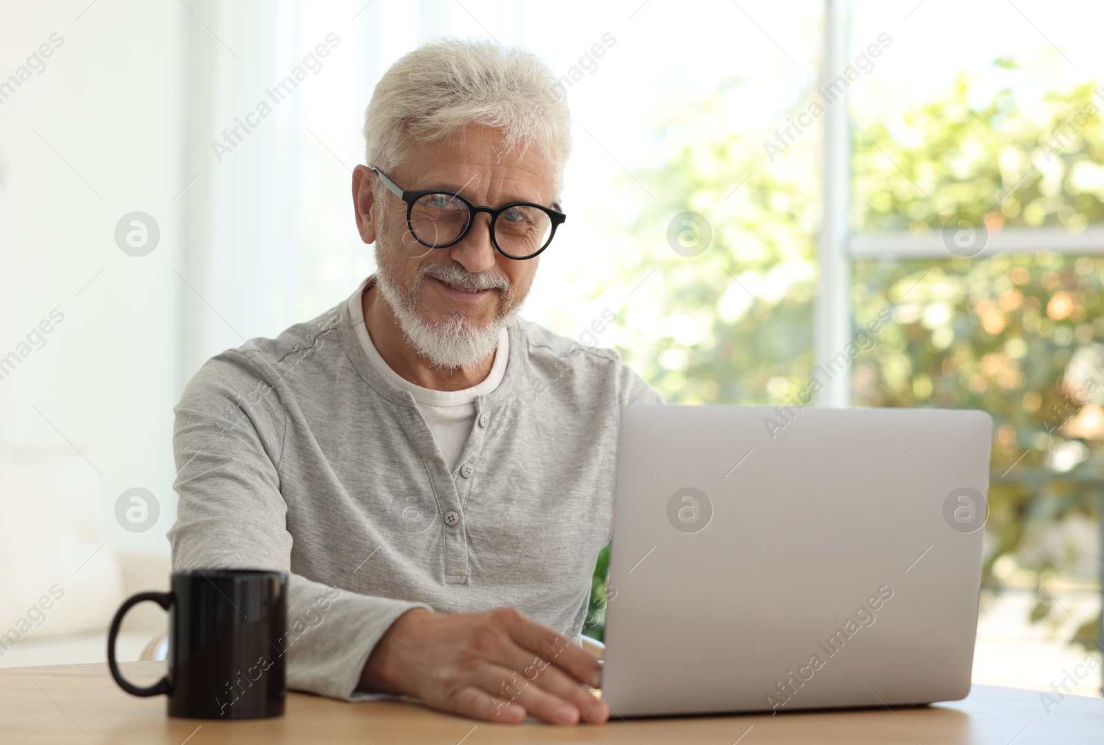 Photo of Senior man using laptop at table indoors