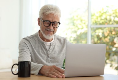 Senior man using laptop at table indoors