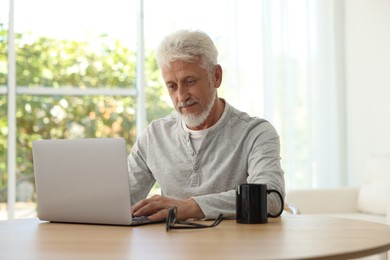 Senior man using laptop at table indoors