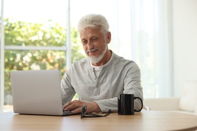 Senior man using laptop at table indoors