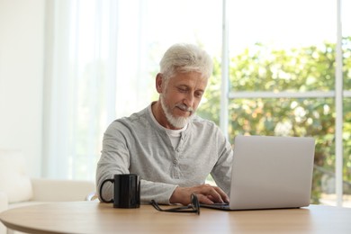 Senior man using laptop at table indoors