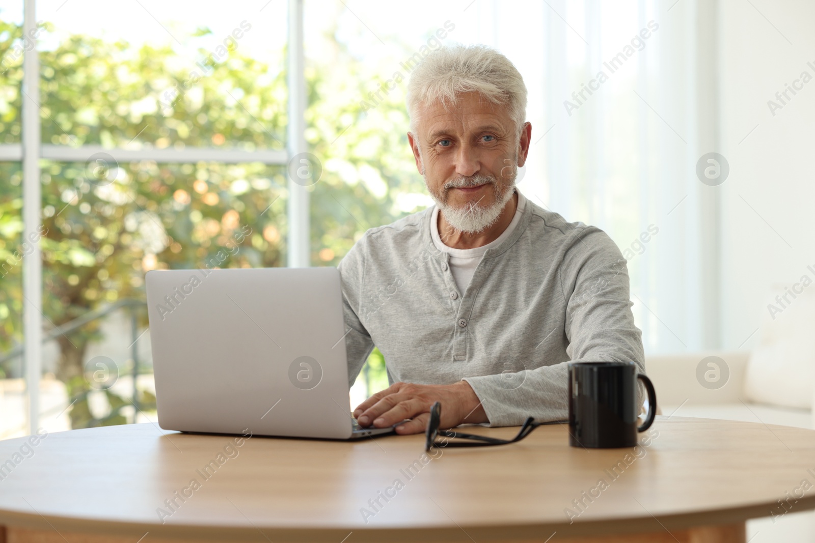 Photo of Senior man using laptop at table indoors