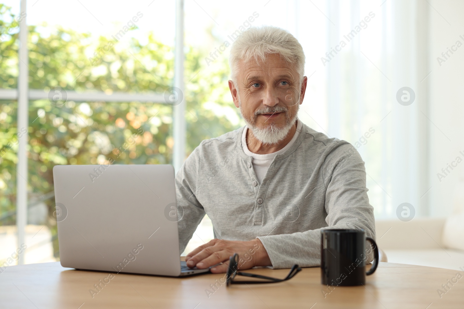 Photo of Senior man using laptop at table indoors