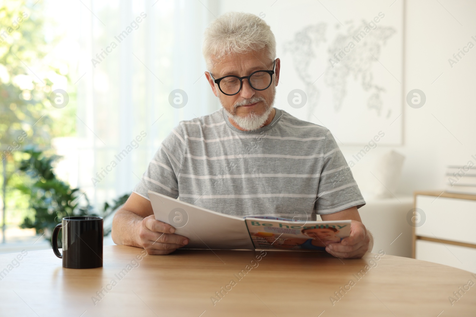 Photo of Senior man reading magazine at table indoors