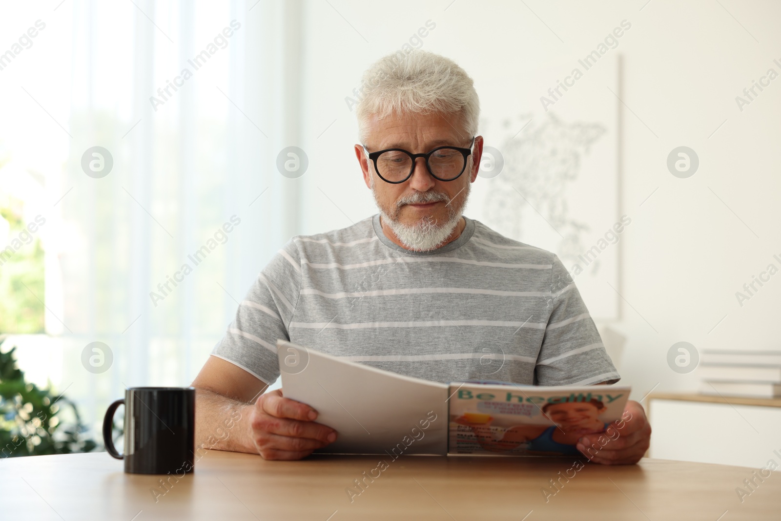 Photo of Senior man reading magazine at table indoors