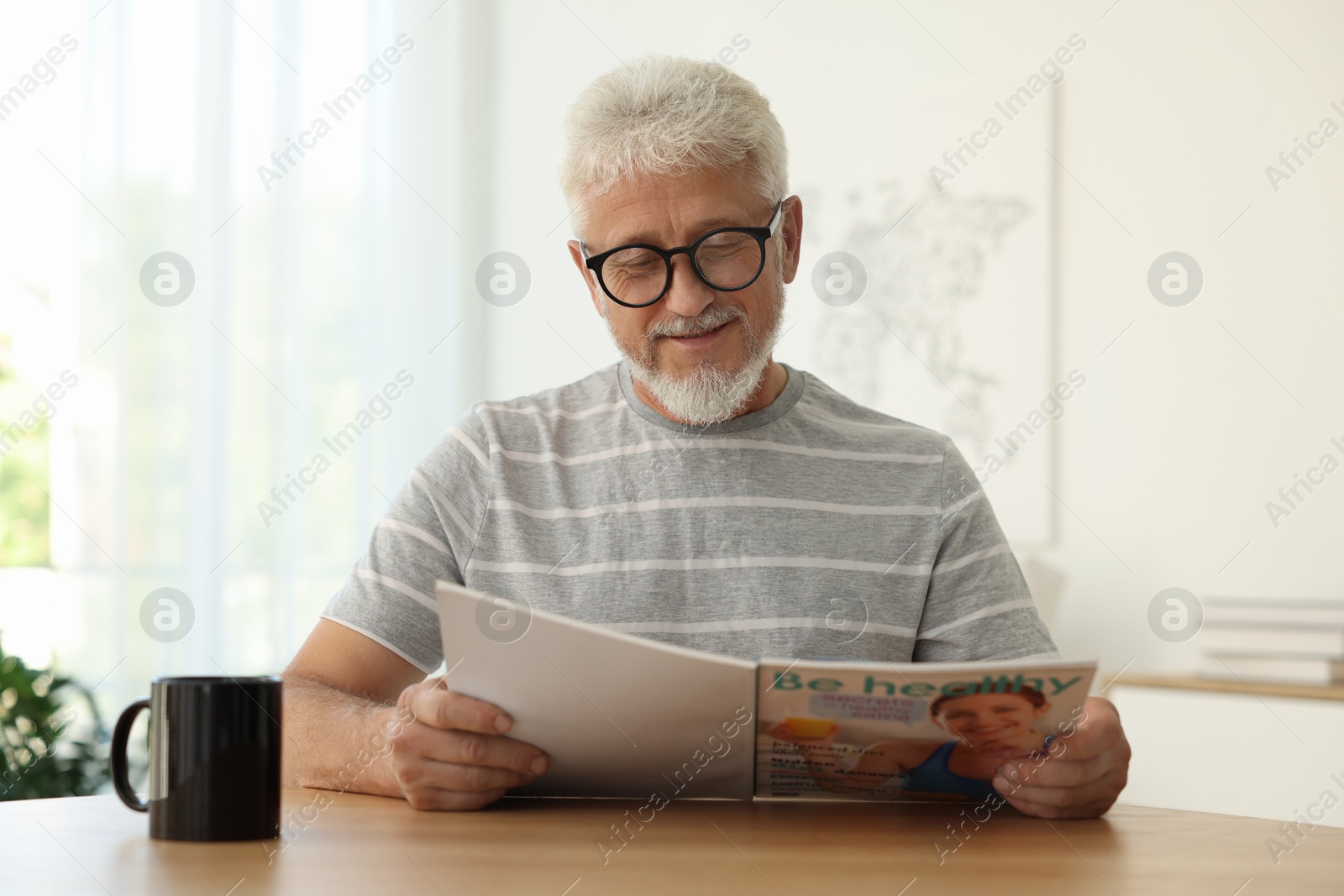 Photo of Senior man reading magazine at table indoors