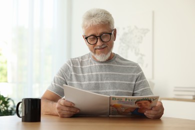 Senior man reading magazine at table indoors