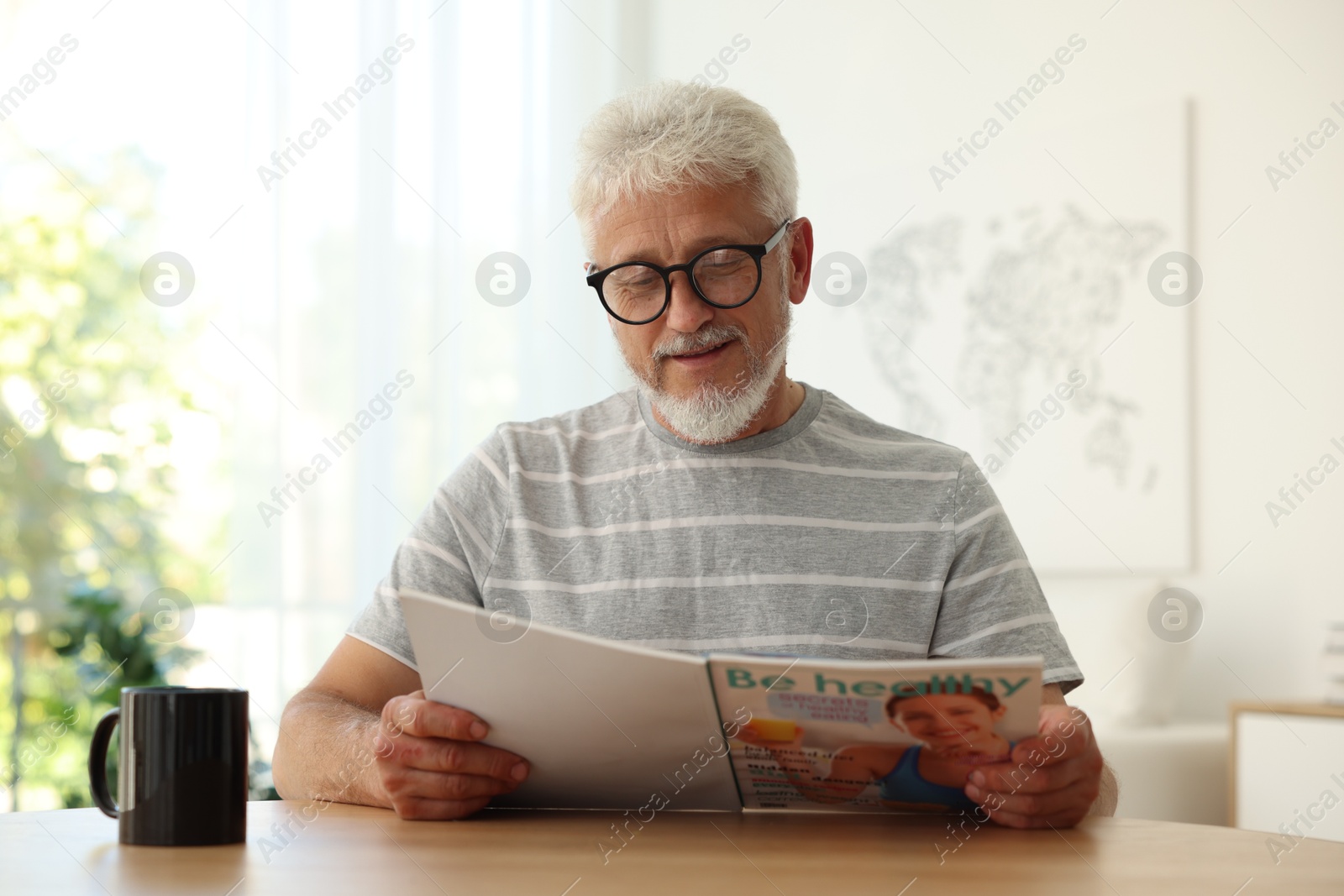 Photo of Senior man reading magazine at table indoors