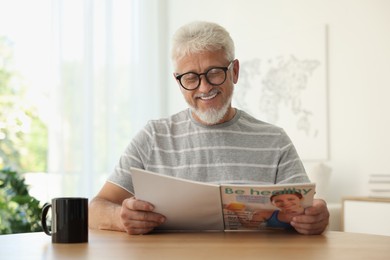 Photo of Senior man reading magazine at table indoors