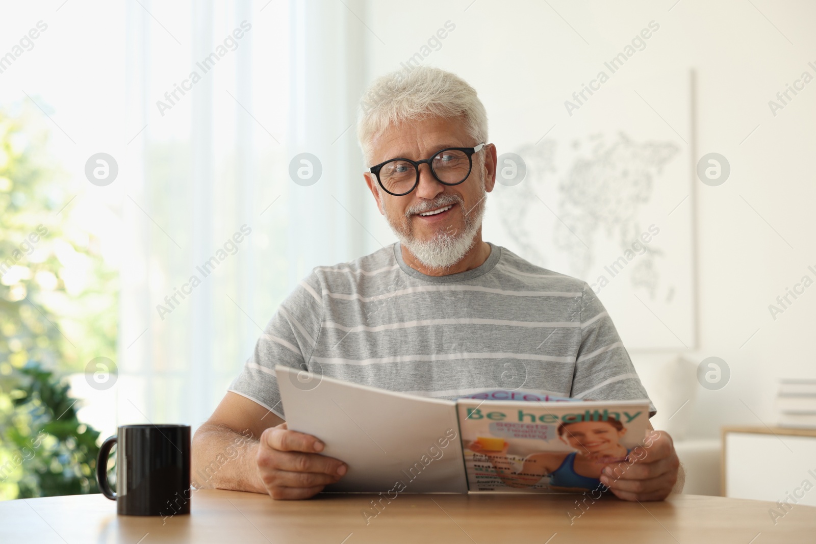 Photo of Senior man reading magazine at table indoors