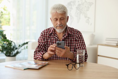 Senior man using smartphone at table indoors