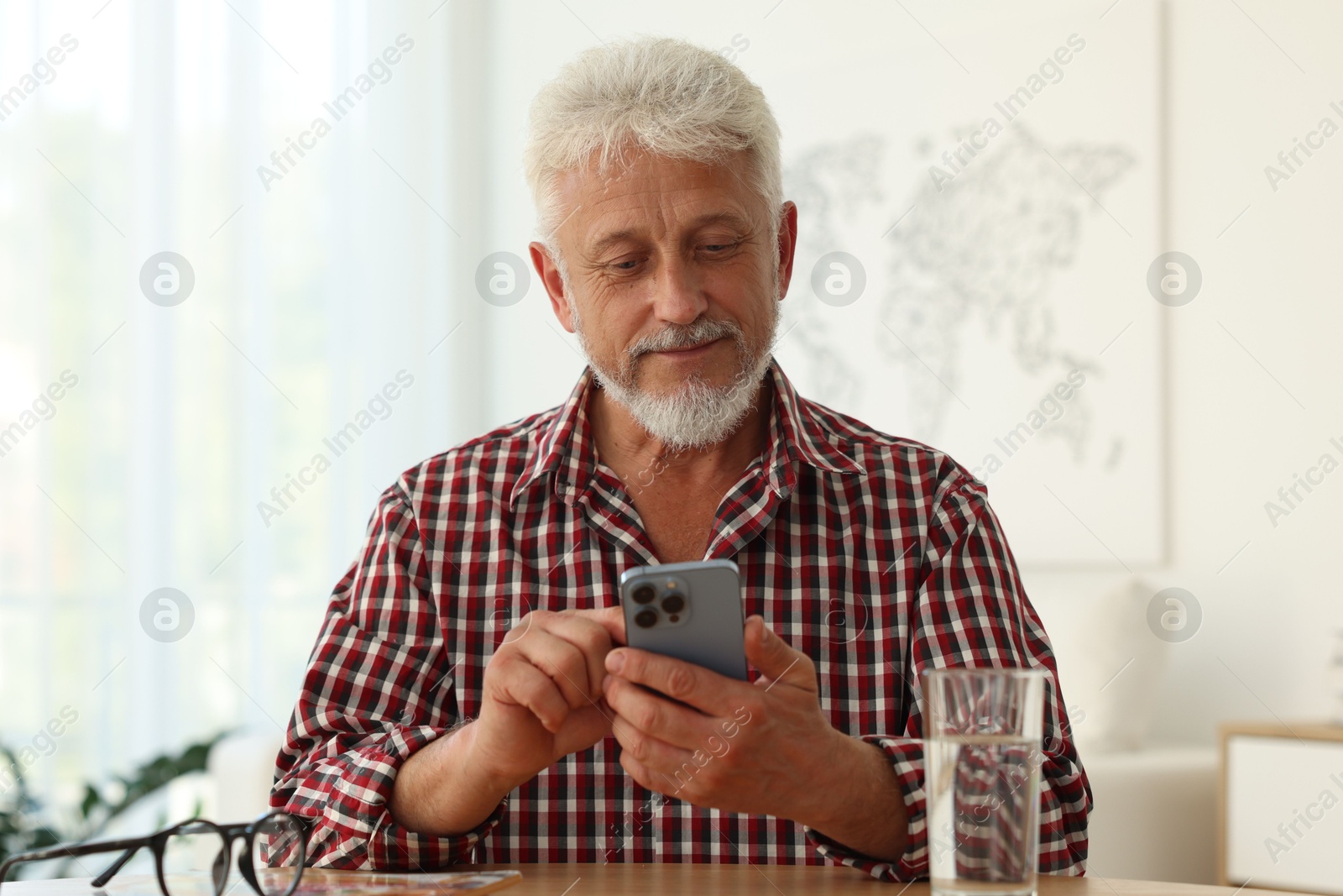 Photo of Senior man using smartphone at table indoors